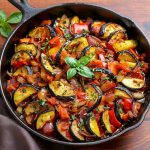 En stekpanna med ugnsbakad ratatouille som innehåller skivade grönsaker som zucchini, paprika och tomater.