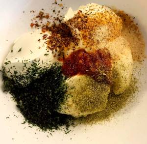 Skål med gräddfil och olika kryddor för tonfiskröra, inklusive dill och paprika.