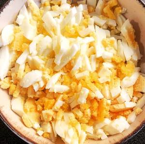 En skål med hackade kokta ägg, både vita och gula bitar blandade.