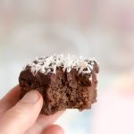 En bit kaka med chokladfrosting och kokosflingor som hålls i en hand.
