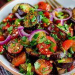 En skål med aubergine och tomater blandat med lök och örter.