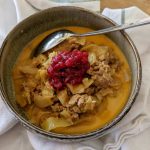 Skål med kål- och köttgryta toppad med lingonsylt och en sked.