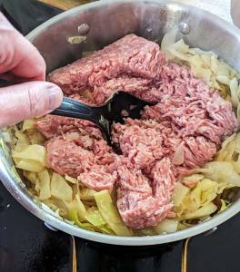 En hand som rör om i en kastrull med köttfärs och kål.