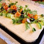 Cheesecake med lax, gurka, tomater och örter på en svart plåt.