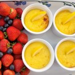 Fyra vita skålar med citronpudding och citronskivor, omgivna av färska bär.