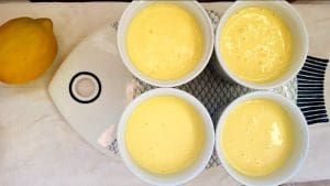 Fyra skålar med citronpudding placerade på en vit tallrik bredvid en citron.