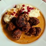 En tallrik med köttbullar i gräddsås och blomkålspuré, dekorerad med lingon.