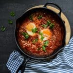 Stekpanna med två ägg i tomatsås, garnerad med färsk persilja och riven ost.