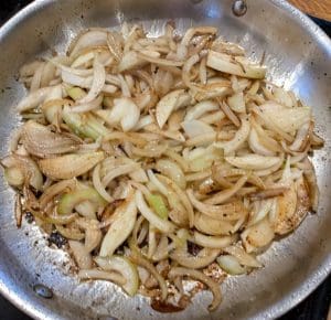 Blandning av stekta lökar i en metallpanna, gyllenbruna och mjuka.