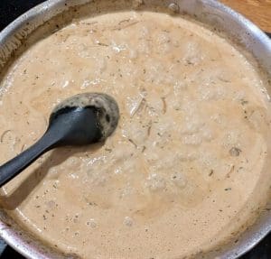 Krämlig gräddsås med svamp och örter i en stekpanna med en slev.
