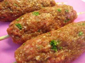 Tre tacospett av köttfärs formade som avlånga bollar med grön örtkrydda.