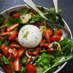 Sallad med burrata, körsbärstomater, spenat och lök i en skål.