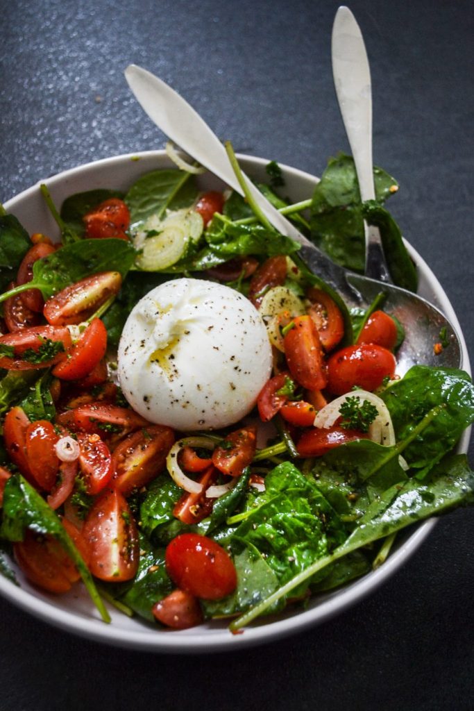 Poké bowl med lax 9 Sallad med burrata, körsbärstomater, spenat och lök i en skål.