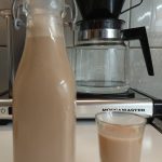 En glasflaska med hemgjord sockerfri Baileys och ett litet shotglas med samma dryck.