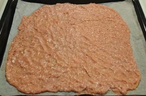 Utbred köttfärs på en plåt med bakplåtspapper, med en jämn och slät yta.