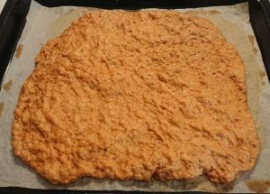 En platt, oregelbunden form av kycklingchips på bakplåtspapper på en plåt.