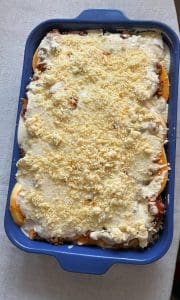 En blå ugnsform med butternut lasagne toppad med ost och brödsmulor.