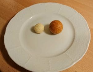 Två friterade ostbollar, en liten vit och en större brun, på en vit tallrik.
