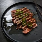 Skivor av halstrad tonfisk på en svart tallrik med sojasås och jalapeños.
