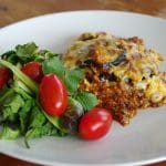 En portion kramig moussaka serverad med en grönsallad och körsbärstomater.