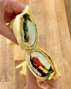 En hand som håller en skuren LCHF-wrap med ost, grönsaker och fyllning.
