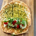 Wrap med pesto, mozzarella, körsbärstomater och ruccola på en träskärbräda.