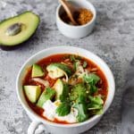 Skål med tacosoppa innehållande avokado, gräddfil, ost och koriander.