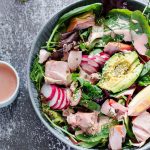 Pokébowl med lax, avokado, rädisor och grönsaker i en skål med dressing vid sidan.
