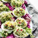 Ägghalvor fyllda med avokado och chili, serverade på en tallrik med grönsaker.
