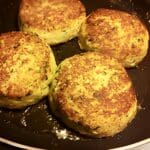 Fyra blomkålsbiffar med parmesan som steks i en panna.