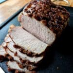Skivad köttbit med en krispig yta, placerad på en svart skärbräda.