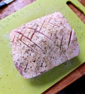 Kryddad köttbit med snitt på en grön skärbräda, täckt av kryddor och salt.