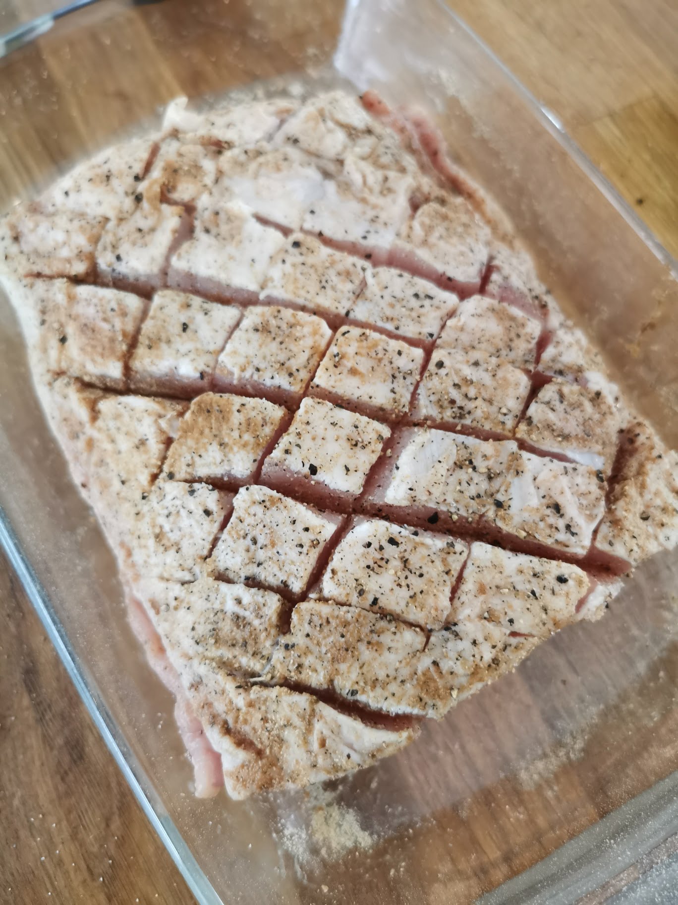 Kryddad fläskköttbit med rutmönster skuren på ytan i en glasform.