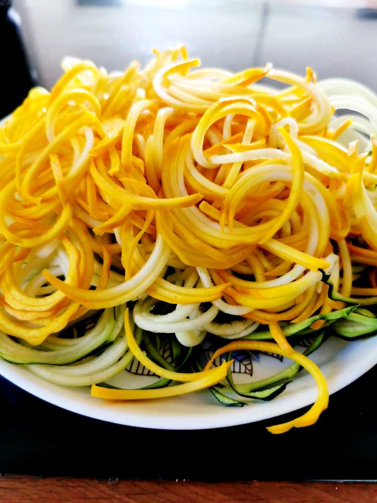 En tallrik med spiraliserade grönsaksnudlar av zucchini och morot i olika färger.
