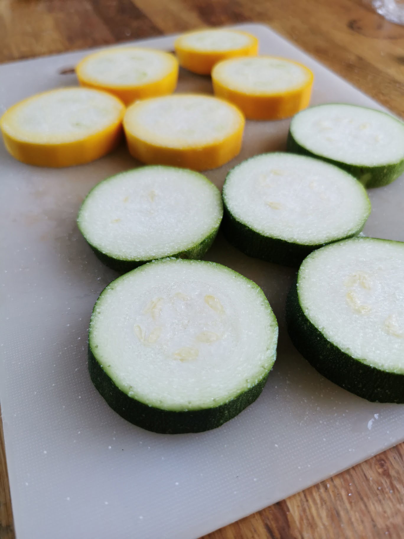 Skivor av gul och grön zucchini placerade på en skärbräda.