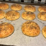 En plåt med nygräddade bröd täckta med vallmofrön på bakpapper.
