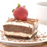 En bit choklad- och gräddtårta med en jordgubbe på toppen, serverad på en tallrik.