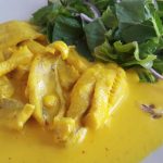 En tallrik med gul curryfisk och en sida av grön sallad med lök.
