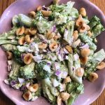 En skål med broccolisallad innehållande broccoli, lök och nötter.