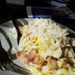 En tallrik med pasta, bacon och riven ost på en mörk bakgrund.
