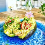 Halverad avokado fylld med en blandning av örter, ost och körsbärstomater på en blå tallrik.