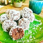 En tallrik med chokladbollar täckta av kokosflingor, med en bit av en boll synlig.