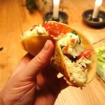 En hand som håller en taco fylld med grönsaker och sås, med ljus i bakgrunden.