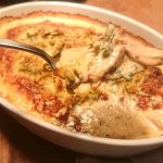En skål med gratäng som innehåller grönsaker och en krämig sås, med en sked som lyfter upp en portion.