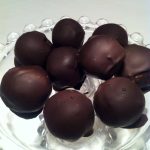 En grupp chokladbollar täckta med mörk choklad placerade på ett glasfat.