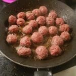 Köttbullar som steks i en svart stekpanna med olja på spisen.