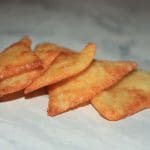 Friterade triangelformade snacks staplade på en ljus yta.