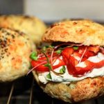 En brödskiva fylld med grönsaker och krämig fyllning, med två bröd i bakgrunden.