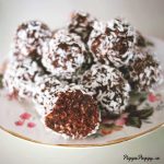 En tallrik med chokladbollar täckta av kokosflingor, placerade på en mönstrad tallrik.