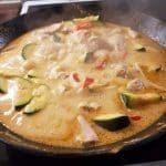 En gryta med kyckling, zucchini och paprika som kokar i en panna på spisen.